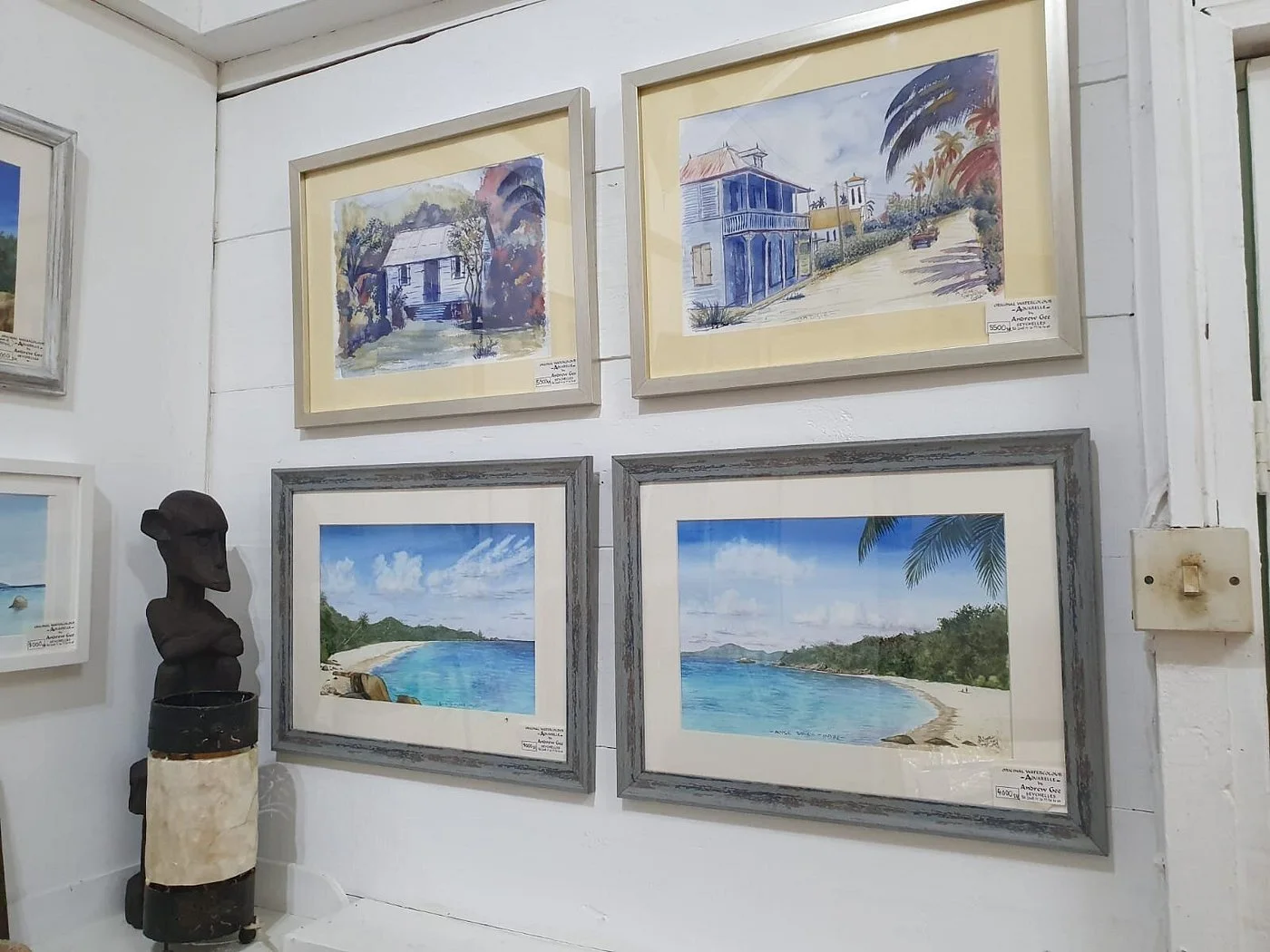 Wall of framed Andrew Gee watercolour paintings of Seychelles houses and beaches — art gallery display at Maison Soleil, Anse Soleil, Seychelles